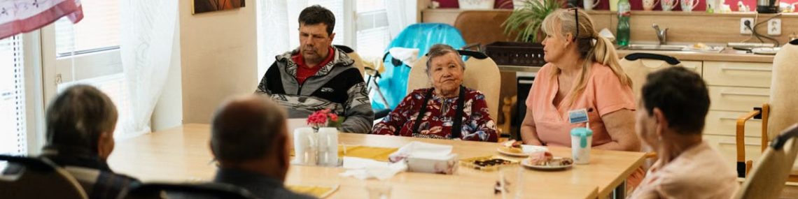 Seniors enjoying a meal in a nursing home dining room with caregivers in Karviná, Czechia.