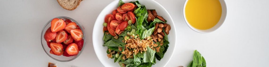 Top view of a healthy salad and fresh ingredients with bread and juice on a white surface.